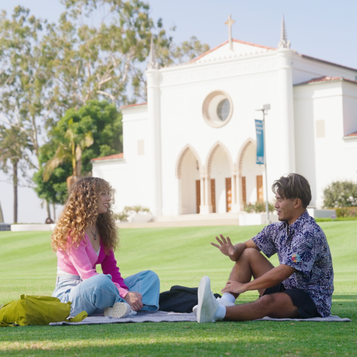 Two students sit talking on LMU's Sunken Garden